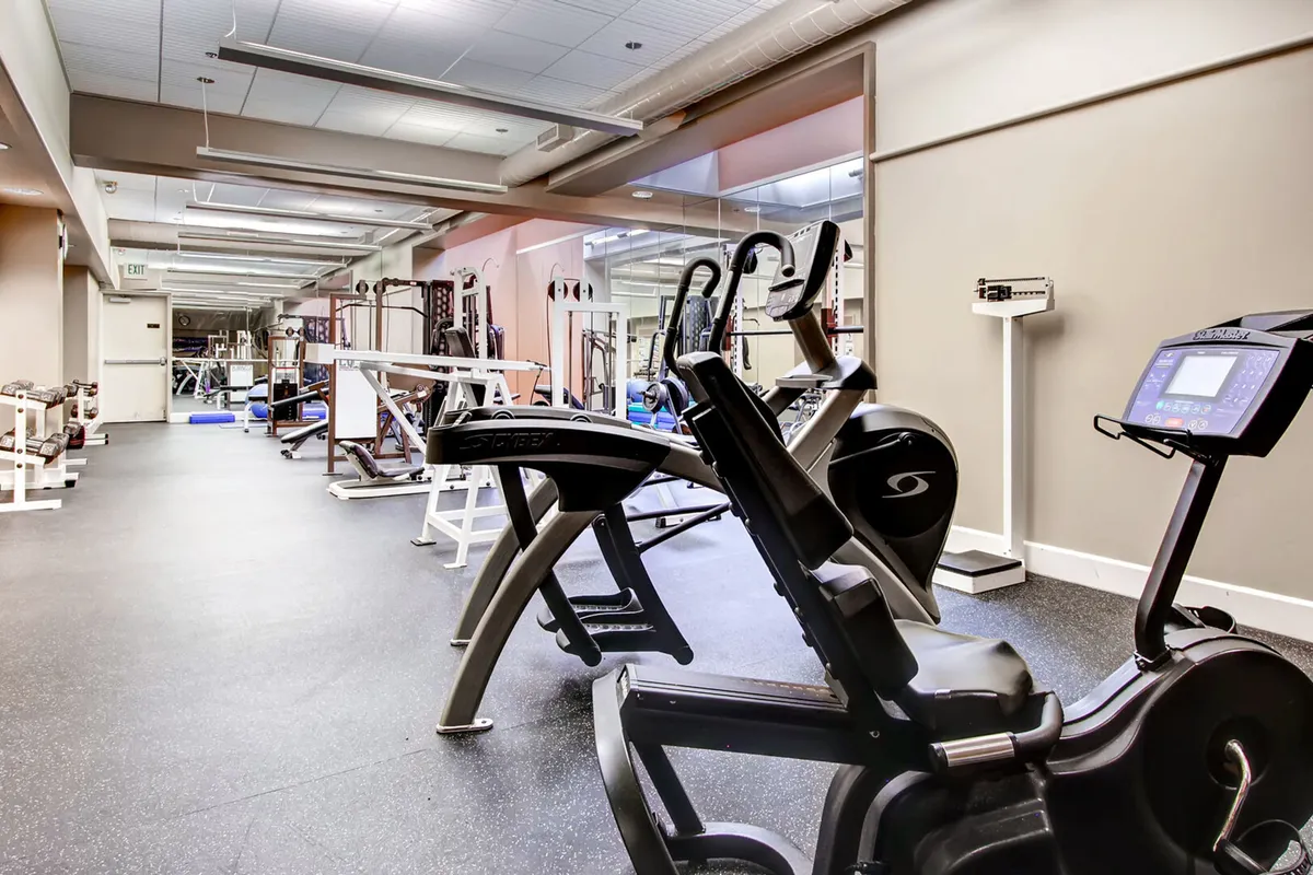 A bright, motivational fitness center equipped with exercise machines, a mirrored wall, and a weightlifting area. The layout invites strength training, cardio workouts, and social fitness activities, supporting guests in maintaining their routines while away from home.