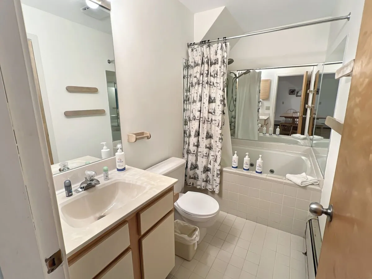A bathroom with a jetted bathtub, sink, shower curtain, and toilet. The mood is calm and inviting, suggesting opportunities for relaxation and self-care, such as enjoying a soothing soak after a day outdoors.