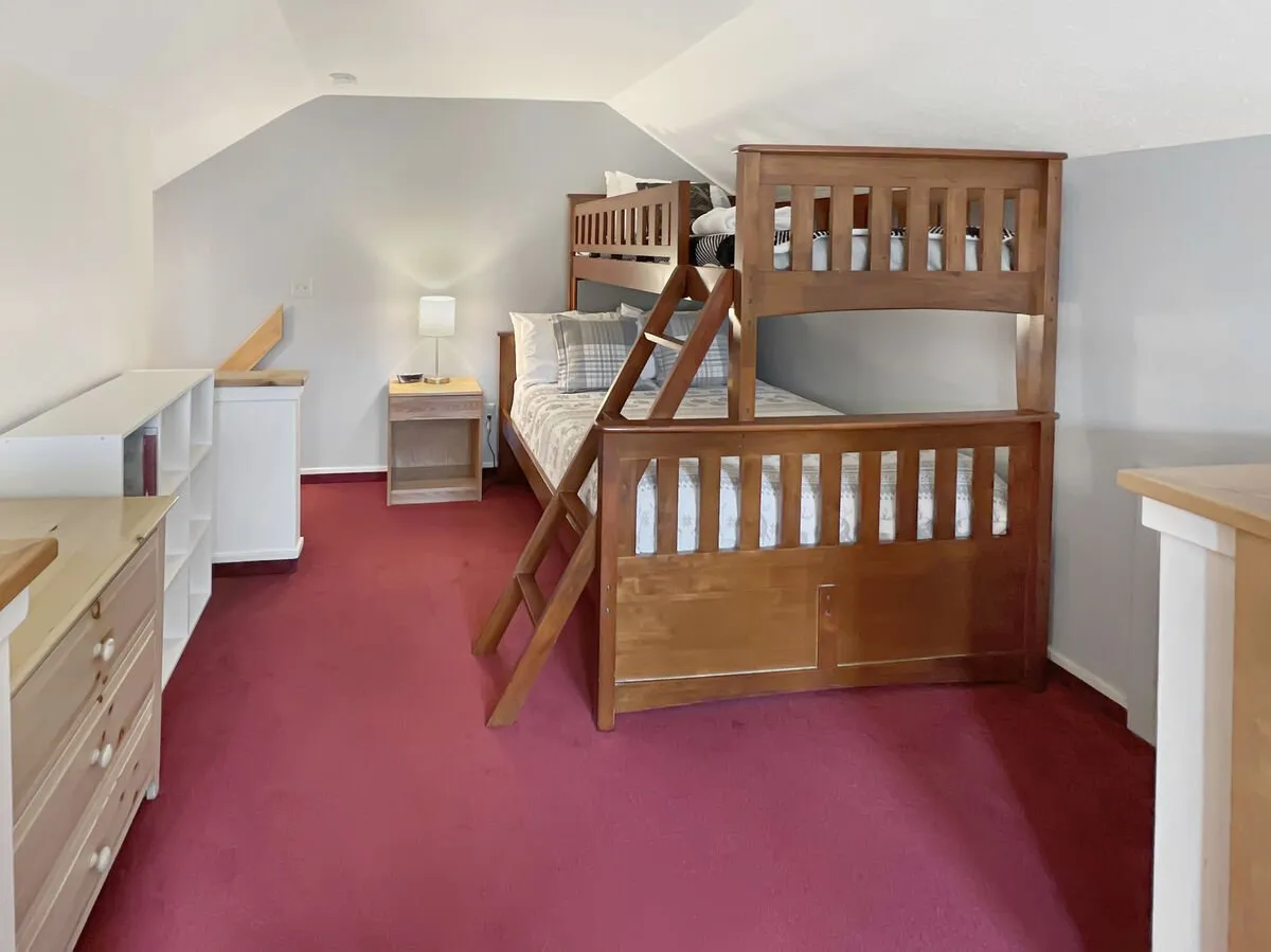 A cozy nook with bunk beds, a nightstand with a lamp, and a dresser. The inviting decor and playful atmosphere emphasize the room's suitability for children or extra guests, with space for both sleeping and low-key play or reading.